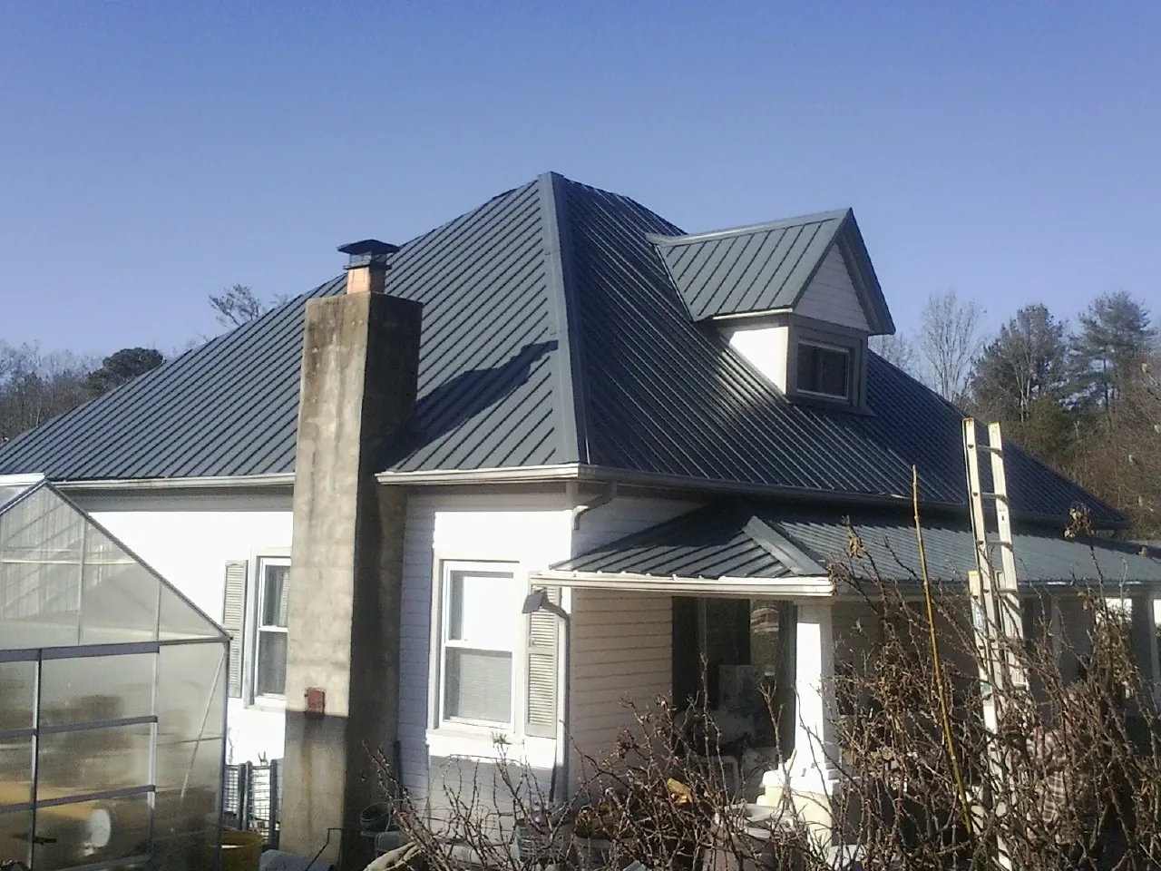 Dark blue standing seam metal roof on a white farmhouse with dormer — Slate & Tile Roof Repair by Roofing Brothers in Avella