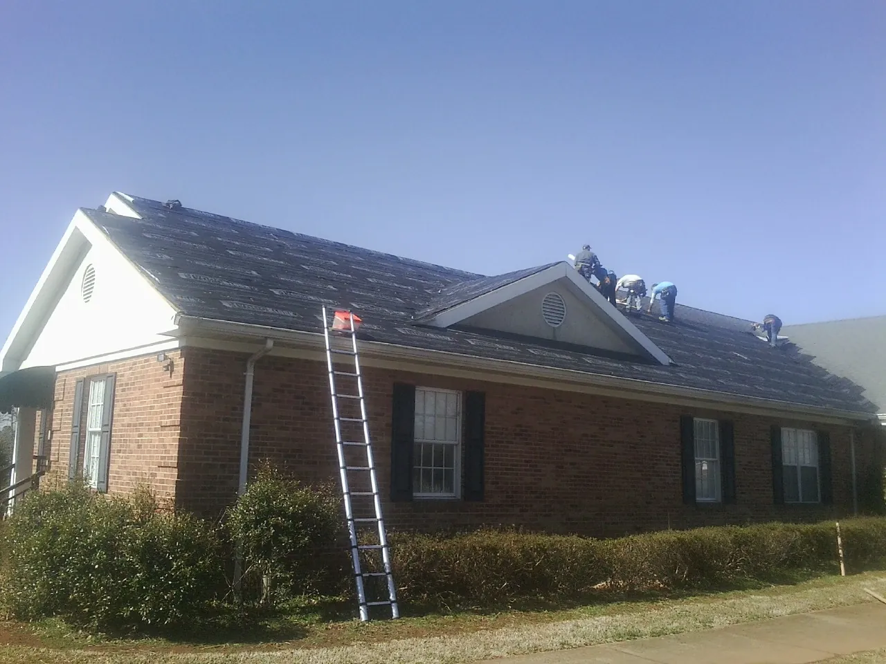 Crew tearing shingles off a brick ranch roof with a ladder set — Emergency Roof Repair work by our crew in Avella