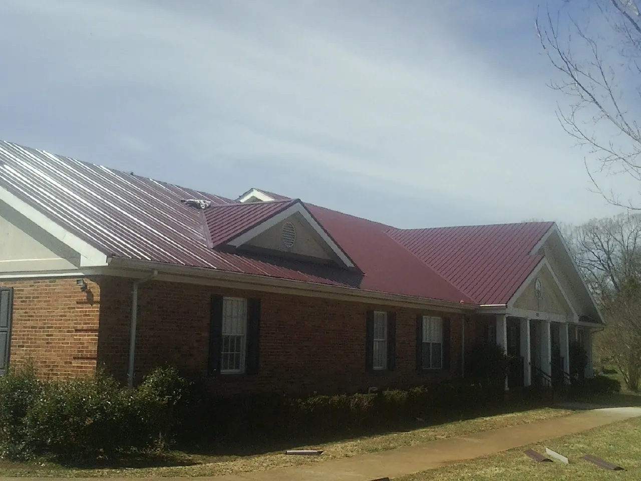 Red metal roof with gabled entries on a long brick building, from a Hail Damage Roof Repair job in Avella