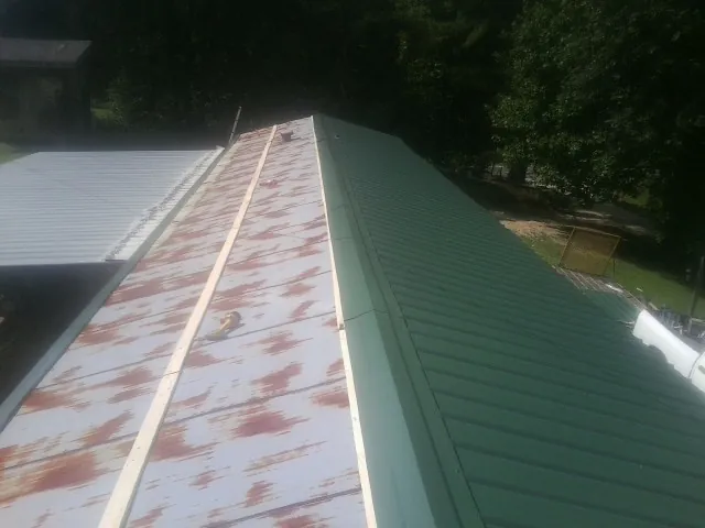 Old rusted panels beside newly installed green metal roofing — Wind Damage Roof Repair by Roofing Brothers in Avella