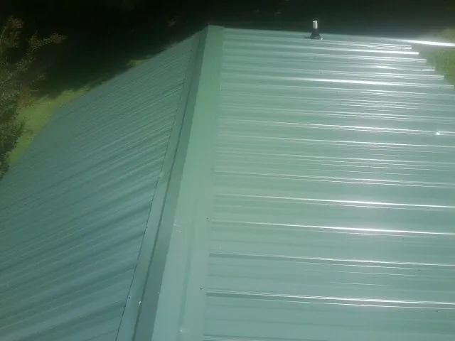 New green metal panels meeting at the ridge of a roof — Flat Roof Repair work by our crew in Avella