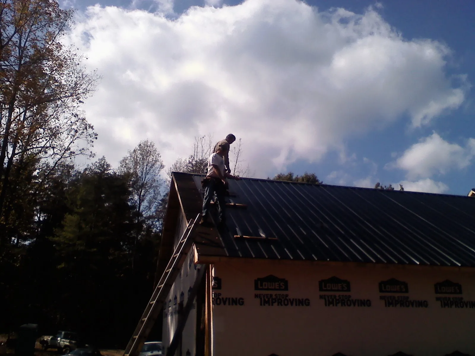 Roofer fastening dark metal panels high against a cloudy sky, from a Roof Inspection job in Avella