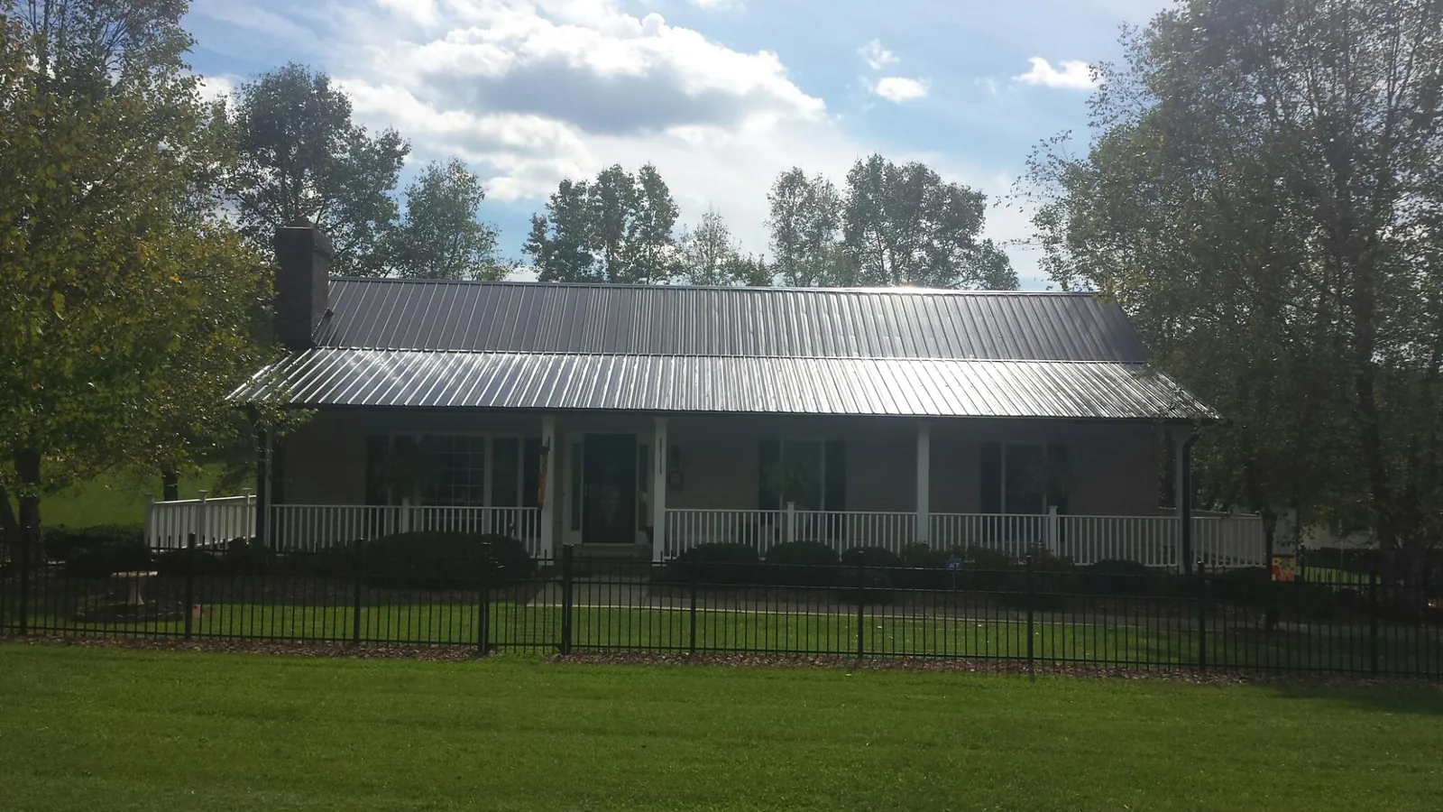 Gray metal roof on a brick ranch with a full width front porch — Gutter Guard Installation work by our crew in Avella